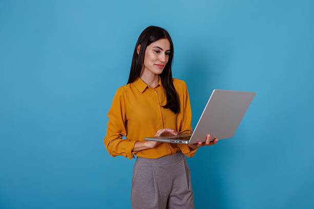 istock Entrepreneur woman using laptop, typing on keyboard and smiling, standing against blue background 2245635216