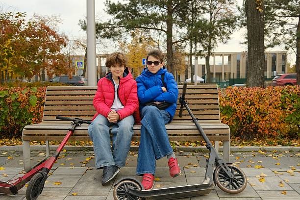 Brothers sitting on a bench for resting after riding scooter, brotherhood, friendship, autumn, lifestyle