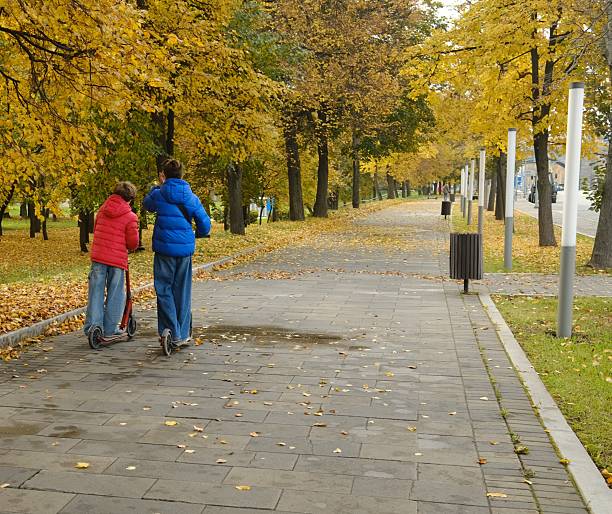 Two brothers riding scooter in park in autumn, autumn colors, city park
