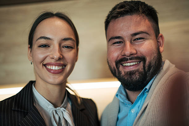 Two smiling business colleagues — man and woman — standing side by side in a studio office portrait, projecting teamwork, confidence, positivity and professional success