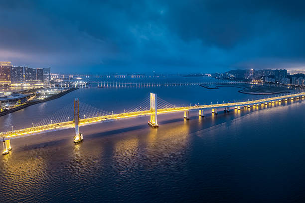 istock Aerial night view of the beautifully illuminated cable-stayed bridge spanning the sea under a dramatic cloudy blue sky in Macau. 2245643790