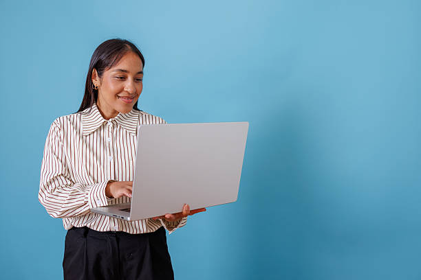 istock Businesswoman standing and working on laptop, smiling with focus while using technology on blue background 2245649098