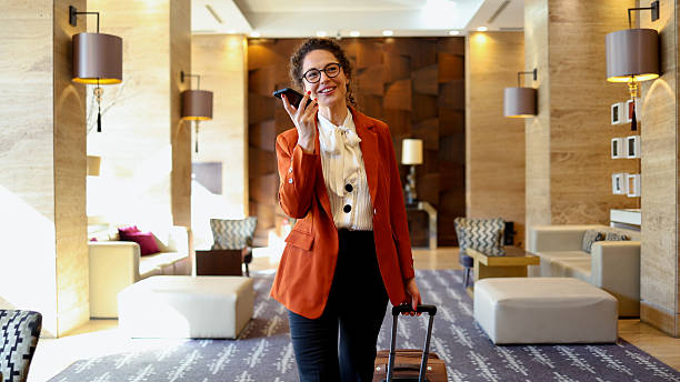 istock Professional businesswoman using voice assistant on mobile phone in luxury lobby. She is traveling for work 2245649821