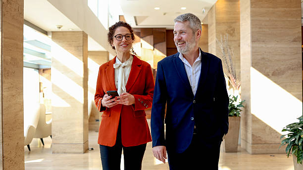 istock Business colleagues walking and talking in hallway, discussing work, holding smartphone, smiling, teamwork, corporate 2245650121