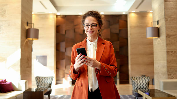 istock Professional businesswoman smiling while using smartphone in modern hotel lobby, networking during business travel 2245650673