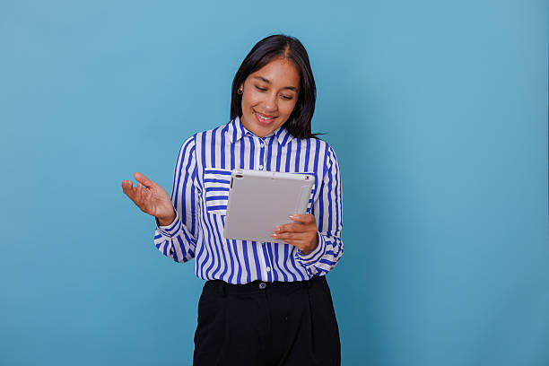 istock Professional woman using tablet for video call, feeling happy and gesturing while standing against blue background 2245652423