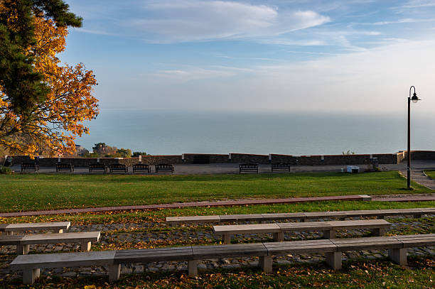 A peaceful viewpoint in Tihany offers a stunning panorama of Lake Balaton. Wooden benches and autumn-colored trees frame the calm blue water under a clear sky, creating a serene and contemplative atmosphere.