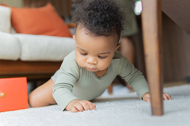 istock Curious infant in green one-piece crawls on carpeted living room floor, exploring and learning through play 2245659576