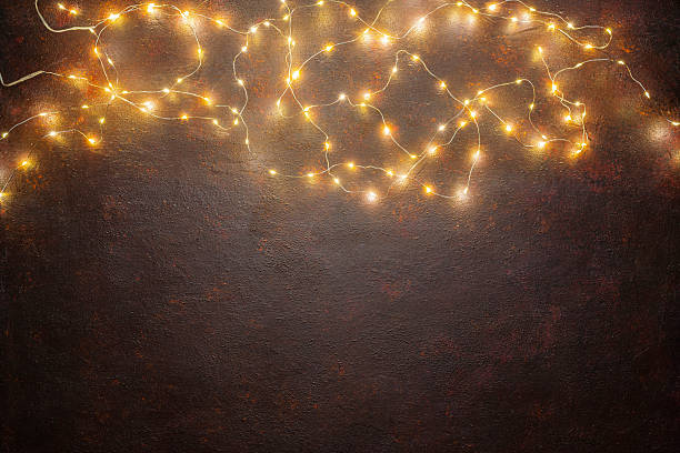 Illuminated brown background by glowing string lights arranged at the top of the frame. Flat lay with copy space. Festive greeting card