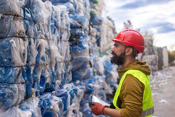 istock Bearded worker at a recycling facility inspecting large bales of compressed plastic waste 2245672298