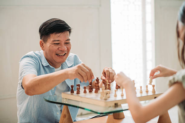 istock Asian chinese father smiling while playing chess with daughter at home on small glass coffee table 2245673385