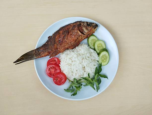 Fried fish with white rice and vegetable on wooden plate with wooden table background. Flat lay