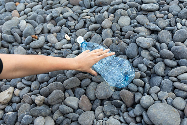 Hand picking up a plastic water bottle from a pebble beach, contributing to ocean cleanup efforts