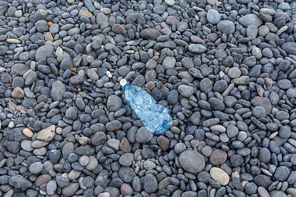 Used plastic bottle discarded on a pebble beach, illustrating environmental pollution and waste