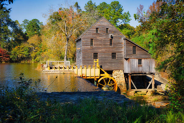 A nice landscape in Autumn of the historical timber gristmill with a new waterwheel and the shadowy pond waters at Yates Millpond Park in Raleigh, North Carolina in the Eastern United States.