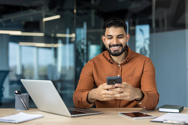 istock Young smiling businessman using smartphone in modern office 2245687212