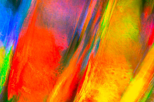 A bold abstract close-up shows vivid streaks of red, yellow, green, and blue blending into fiery shapes, creating a glowing, fluid pattern across a smooth, reflective surface.