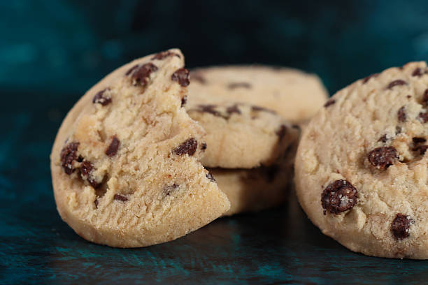 istock Close-up image of halved chocolate chip shortbread round leaning against stack of two choc chip shortcake biscuits, mottled blue-green background, focus on foreground 2245693216
