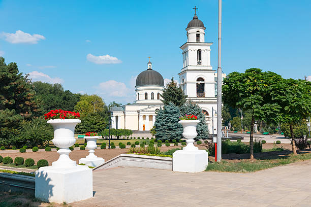 Nativity Cathedral in Chisinau park, framed by trees and neoclassical architecture on a sunny day. White urn planters line the pathway leading to this historic Moldovan landmark and spiritual center