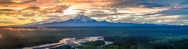 Sunrise illuminates Drum Mountain and Wrangell-St. Elias National Park as seen from Denali National Park and Preserve in Alaska. The River of Light reflects the sky's vibrant colors, creating a stunning vista.