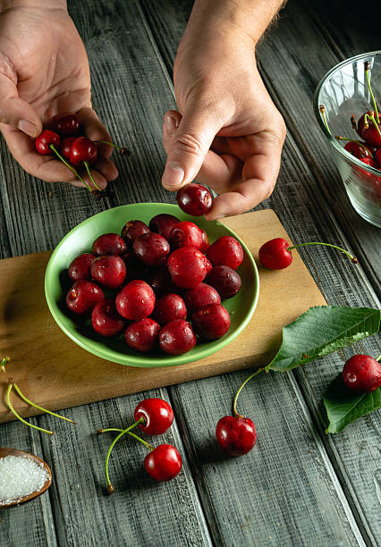 istock Two hands carefully select fresh cherries from a large green bowl placed on a wooden table. The setting features natural light, highlighting the rich colors of the cherries 2245708962