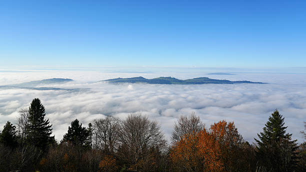 Clouds blanket the valley, revealing mountain peaks under a bright blue sky during autumn