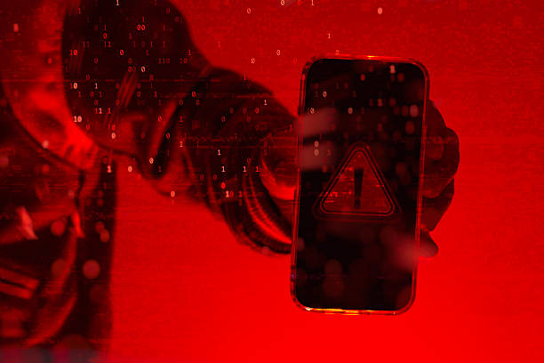 istock Cybercrime and mobile security threat concept. Anonymous hacker holding smartphone with digital warning sign, red alert background, and binary code overlay. 2245727814