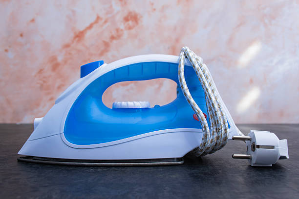 Modern electric iron with blue handle and folded white shirt on a table. Household appliance for laundry, ironing and daily clothing care at home