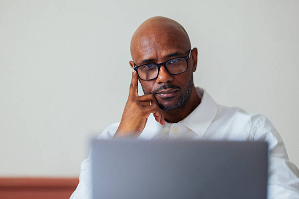 istock Thoughtful Professional Man With Glasses Working On Laptop, Reflective Expression In Modern Office 2245727958