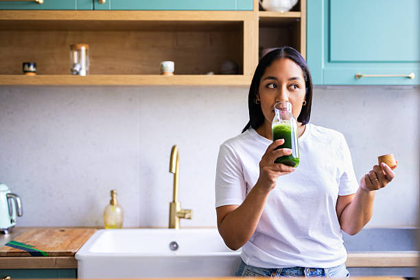 istock Woman Drinking Green Smoothie In Modern Kitchen While Holding Bottle And Snack Cork 2245731178