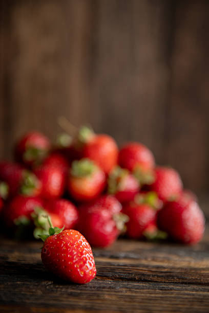 Bright ripe strawberries arranged vertically on rustic dark wood. Simple natural composition for food, health and nutrition themes.