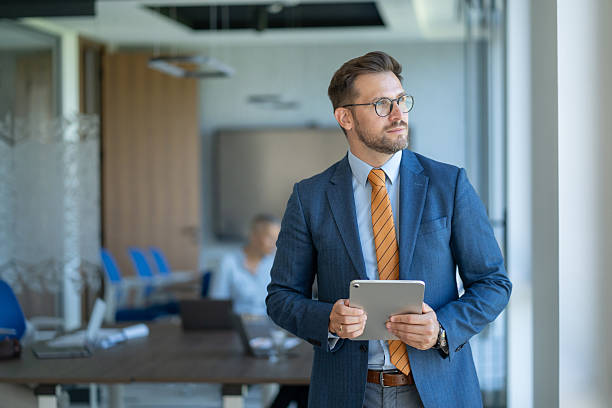 istock Pensive businessman holding digital tablet looking out office window 2245742379