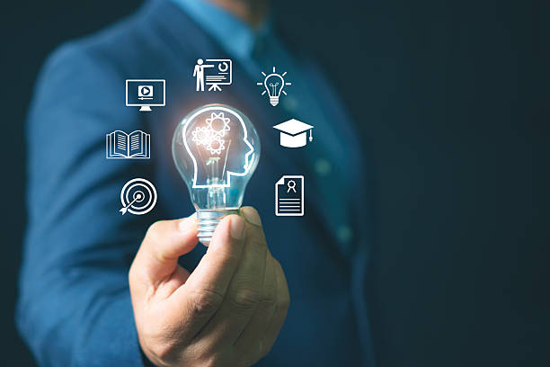 istock Businessman holding light bulb with human head icon and education symbols representing knowledge innovation, learning, e-learning, creativity, idea development, and business training concept. 2245759638