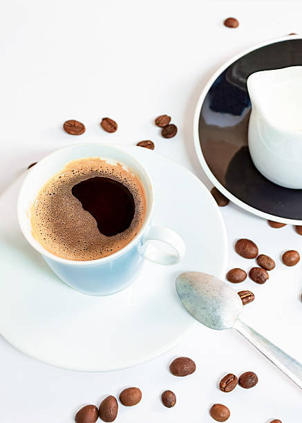 istock Coffee in a blue cup sits on a white table with coffee beans scattered nearby. 2245772700