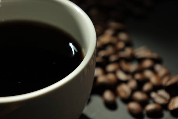Closeup of a coffee cup with coffee beans, roasted coffee beans background, background coffee