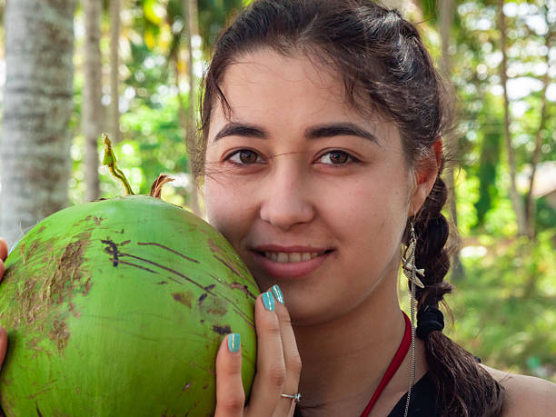 istock Young woman smiling while holding a green coconut outdoors surrounded by tropical trees on a sunny day 2245775429