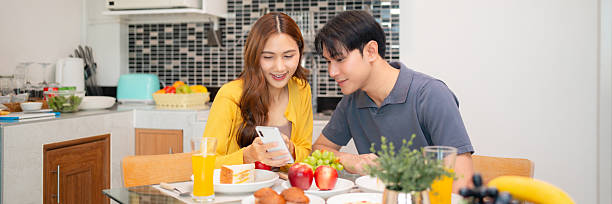 Young pregnant couple having good time at home using mobile phone during breakfast