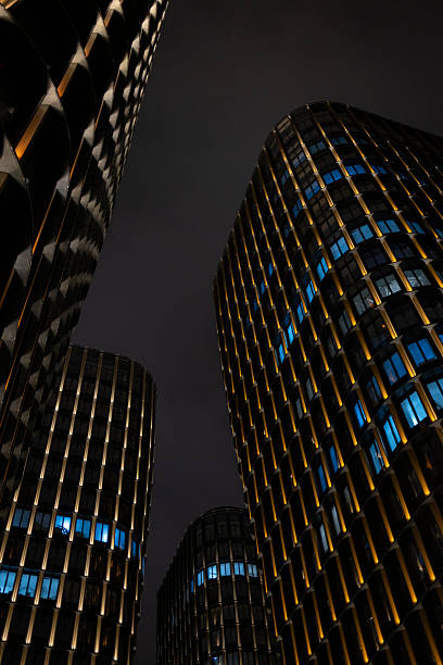 A dramatic low-angle view of modern illuminated skyscrapers. Glowing golden and blue lights create a futuristic and corporate atmosphere against the night sky, symbolizing business and success.