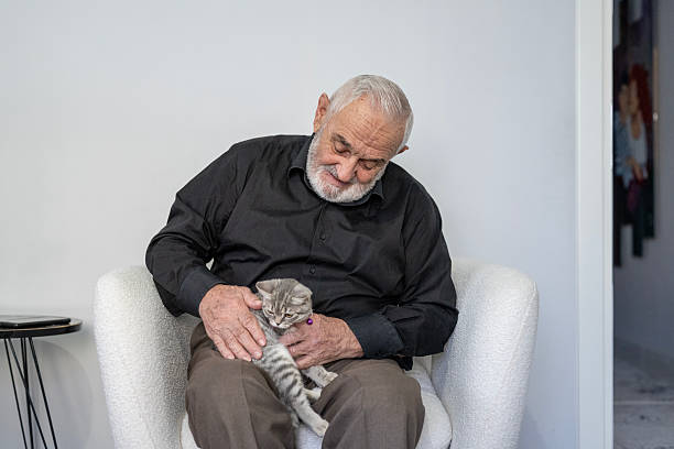An elderly man holds a kitten and smiles to him