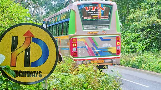 Valparai, Tamilnadu, India - September 28, 2025: A colorful bus navigating a sharp curve on a lush forest road in Valparai, Tamil Nadu, with a highway curve sign in the foreground