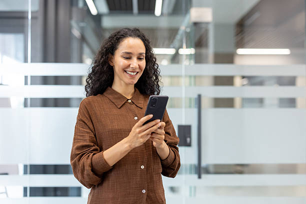istock Smiling woman using smartphone in modern office with glass partitions 2245817493