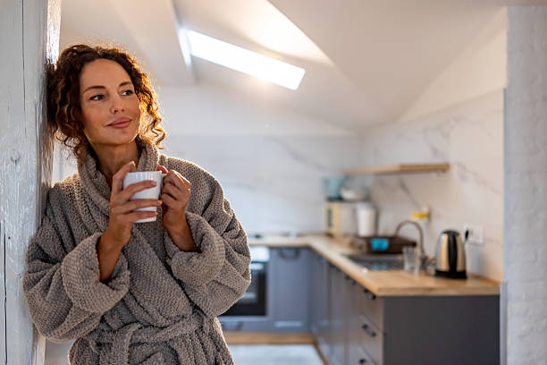 istock Cozy Morning Moment: Woman In Gray Bathrobe Sipping Coffee In Bright Kitchen 2245817866