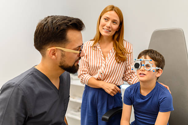 istock Mother standing beside son wearing phoropter while male doctor examines eyes during routine vision checkup at clinic 2245818026