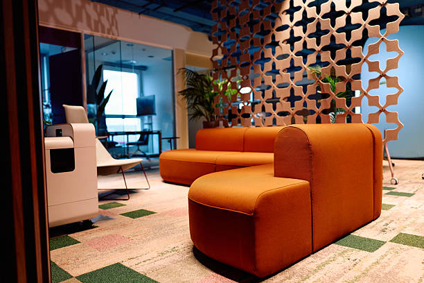 Modern office business interior, black leather sofa in front of a blank white wall. plant, coffee table, conference room in the background. copy space template