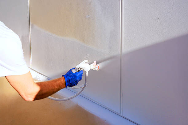 istock Man using spray gun to paint wall indoors in bright lighting during home renovation project 2245820388