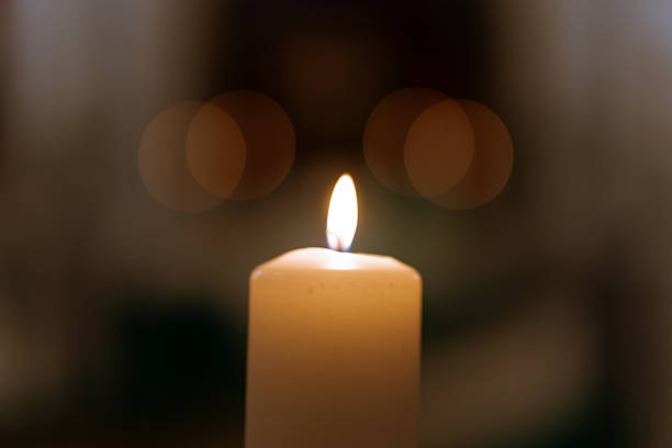 istock Single burning candle with soft bokeh lights  peaceful warm flame symbolizing prayer, remembrance, faith and hope in dark background 2245822770