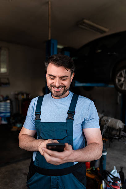 istock Mechanic smiling while checking smartphone in car repair shop during daylight hours 2245830591