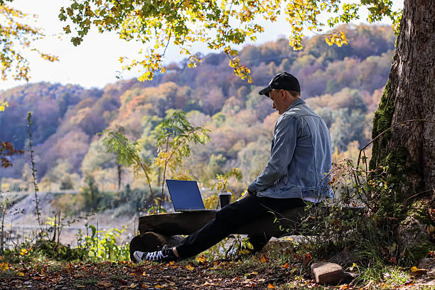 istock Back view of man using laptop on log with coffee in autumn forest 2245833519