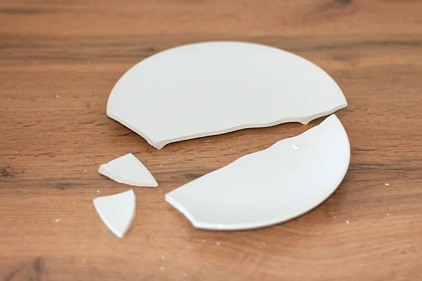 istock A broken white plate on a wooden tabletop, with pieces scattered across the surface. 2245834084