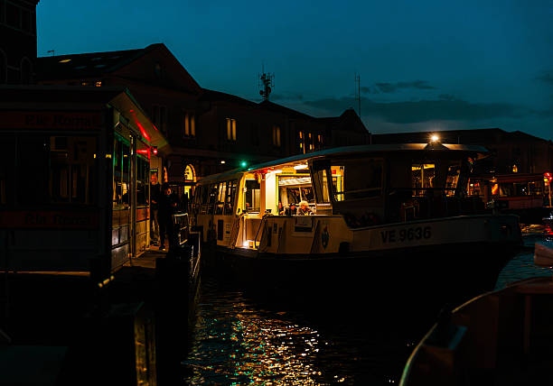 Venice, Italy - November 20, 2024: Illuminated boat is docked at waterfront, surrounded by buildings, creating a tranquil nighttime scene with reflections on water